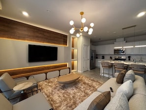 A modern living room with a flat-screen TV, a wooden bench, a round coffee table, and a sofa with cushions. - Resort-style 5 BD/ 4.5 BA/ Windsor Cay - 16209 PF (Clermont)