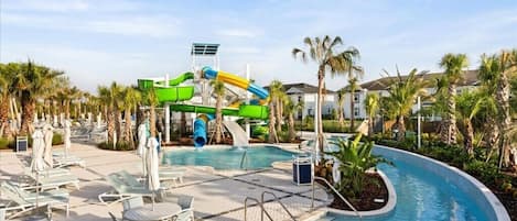 A pool area with a water slide, lounge chairs, and palm trees.