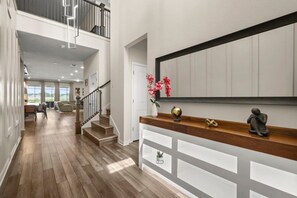 Un intérieur spacieux doté d’un plancher en bois, d’un escalier menant à un niveau supérieur et d’une console blanche agrémentée d’objets décoratifs.