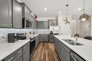 Eine moderne Küche mit grauen Schränken, Edelstahlgeräten, einer weißen Arbeitsplatte und Holzboden.