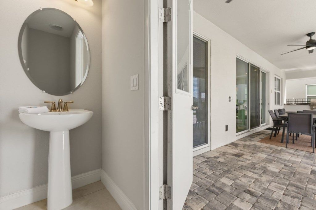 A bathroom with a pedestal sink and a round mirror, a sliding glass door leading to a patio area with a table and chairs.