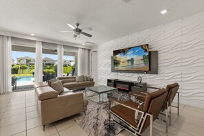 A modern living room with a sofa, coffee table, and TV mounted on a textured wall. - 7 BD / 6.5 BA / Encore Resort at Reunion 256 AA (Kissimmee)