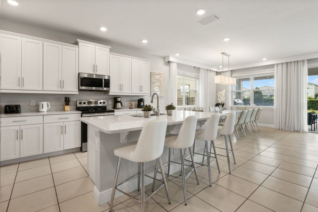 A modern kitchen with white cabinets, a central island with bar stools, and a large window providing a view of the outdoors.