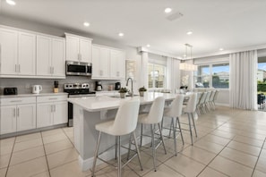A modern kitchen with white cabinets, a central island with bar stools, and a large window providing a view of the outdoors. - 7 BD / 6.5 BA / Encore Resort at Reunion 256 AA (Kissimmee)