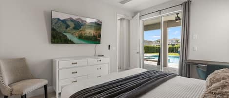 Une chambre avec un lit, une chaise, une commode, un ventilateur de plafond et une grande fenêtre donnant sur une piscine et des montagnes.
