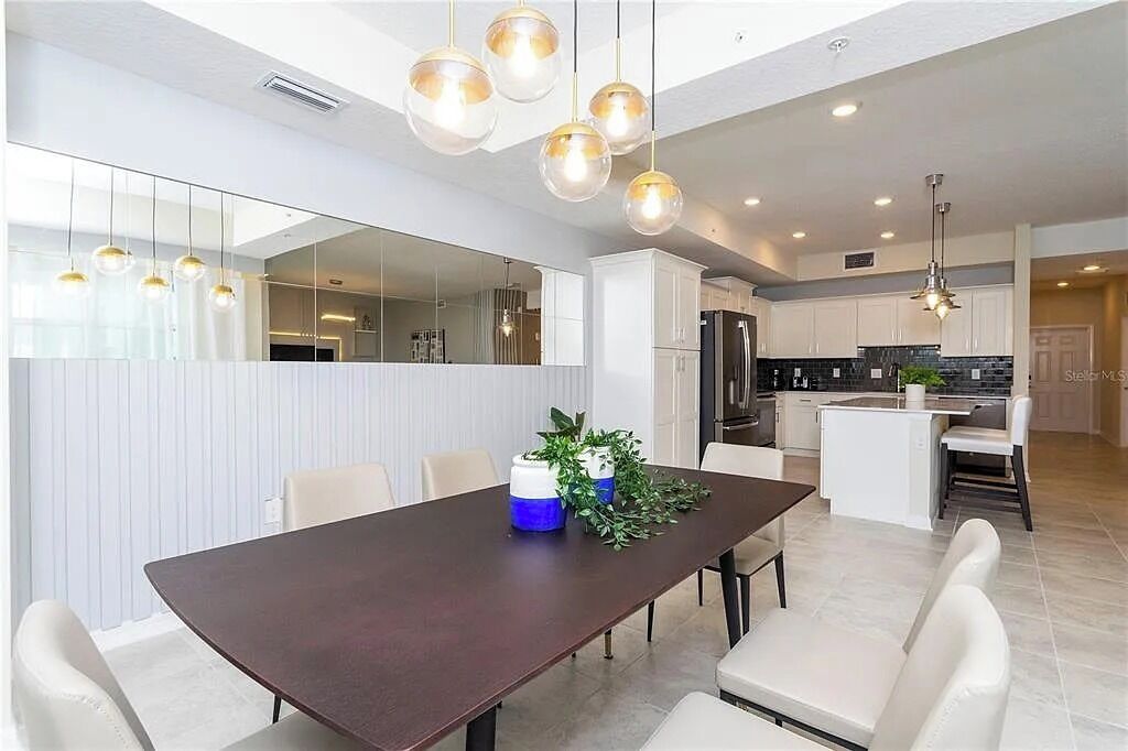 Une cuisine moderne avec des meubles blancs, un îlot central et des luminaires suspendus.