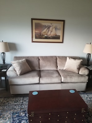 Ein Wohnzimmer mit einem beigen Sofa, zwei Lampen, einem gerahmten Gemälde und einem Holztisch.