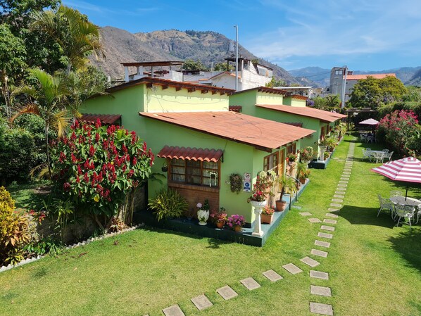 A green house with a red roof, surrounded by a well-maintained garden and a stone pathway leading to outdoor seating.