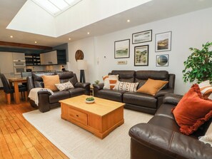 Ein modernes Wohnzimmer mit einer braunen Ledersofa-Garnitur, einem Holztisch und einem Essbereich mit Holztisch und -stühlen.