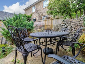 Eine Terrasse im Freien mit einem runden Tisch und vier Stühlen, umgeben von einer Steinmauer und Pflanzen.