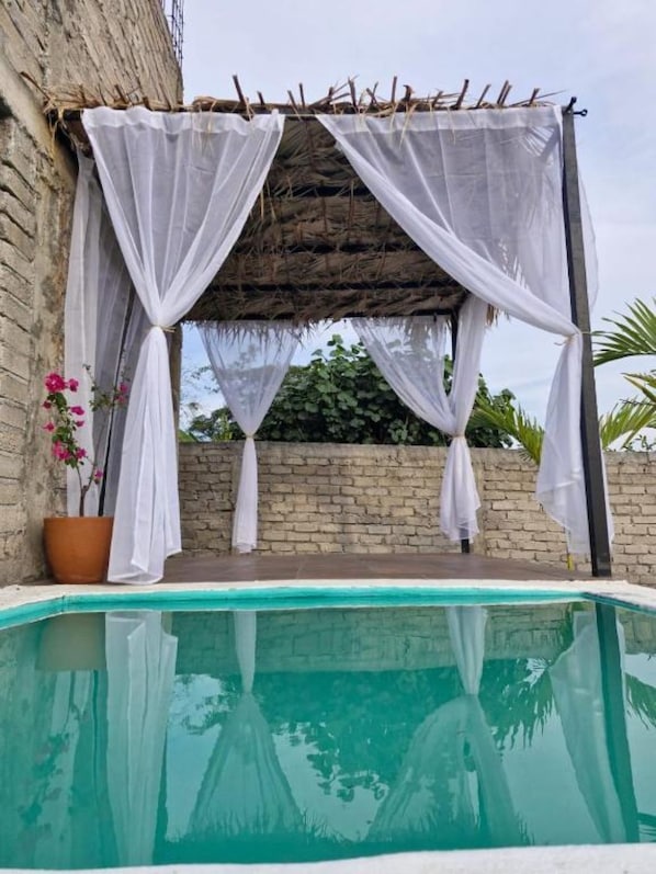 Una zona de piscina con una pérgola, un muro de ladrillo y una planta en maceta.