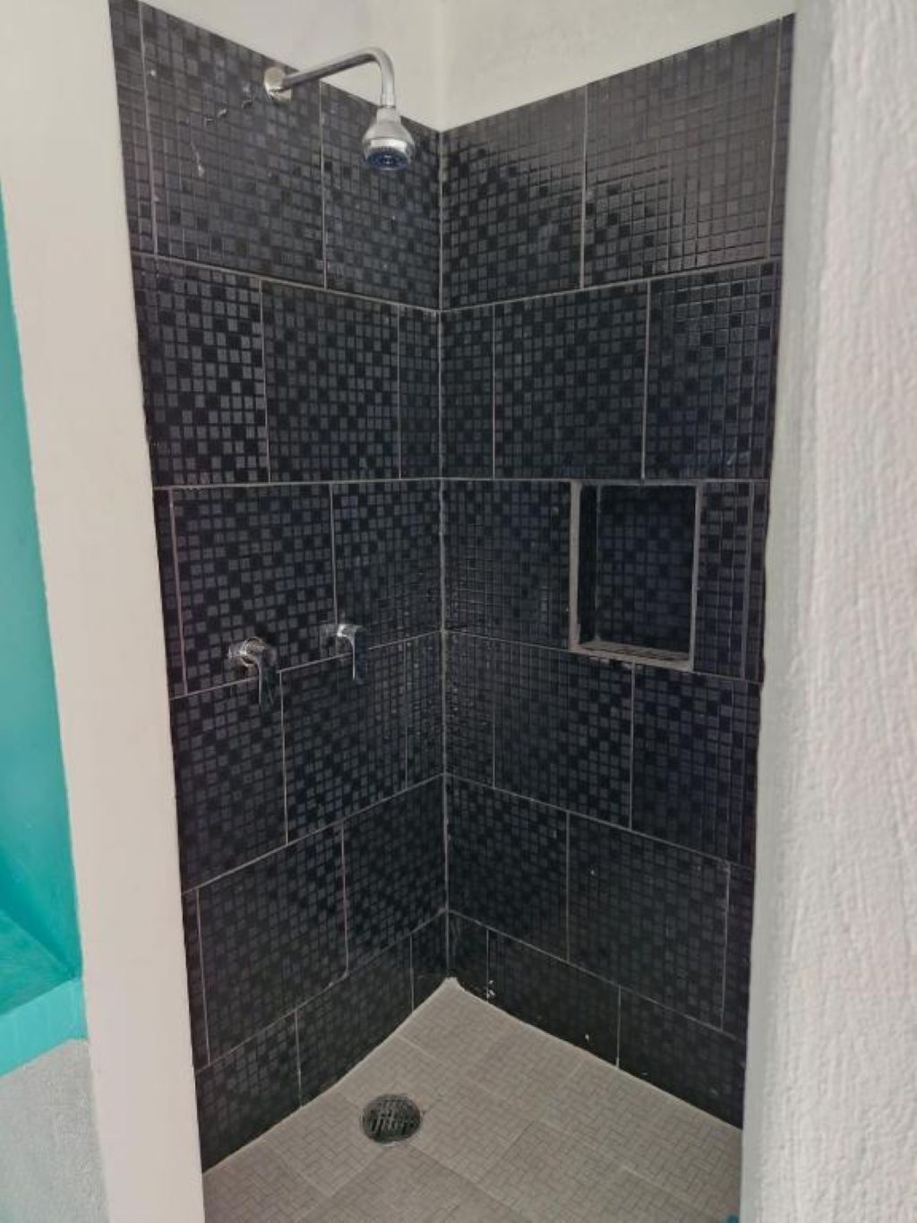 A shower area with dark tiled walls, a showerhead, and a drain.