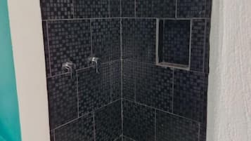A shower area with dark tiled walls, a showerhead, and a drain.