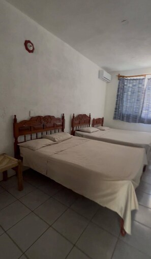 A room with two wooden beds, a small wooden table, and a window with curtains. - Depto. con alberca, Aire Acondicionado y cerca de Carrizalillo, hasta 6 personas (Puerto Escondido)