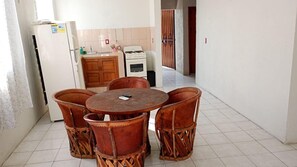 A dining area with a round wooden table and four chairs, a white refrigerator, a stove, and a tiled kitchen backsplash. - Depto. con alberca, Aire Acondicionado y cerca de Carrizalillo, hasta 6 personas (Puerto Escondido)