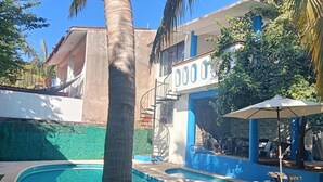 En pool med en böjd kant, omgiven av en grön gräsmatta och en byggnad med blå och vita ytterväggar.