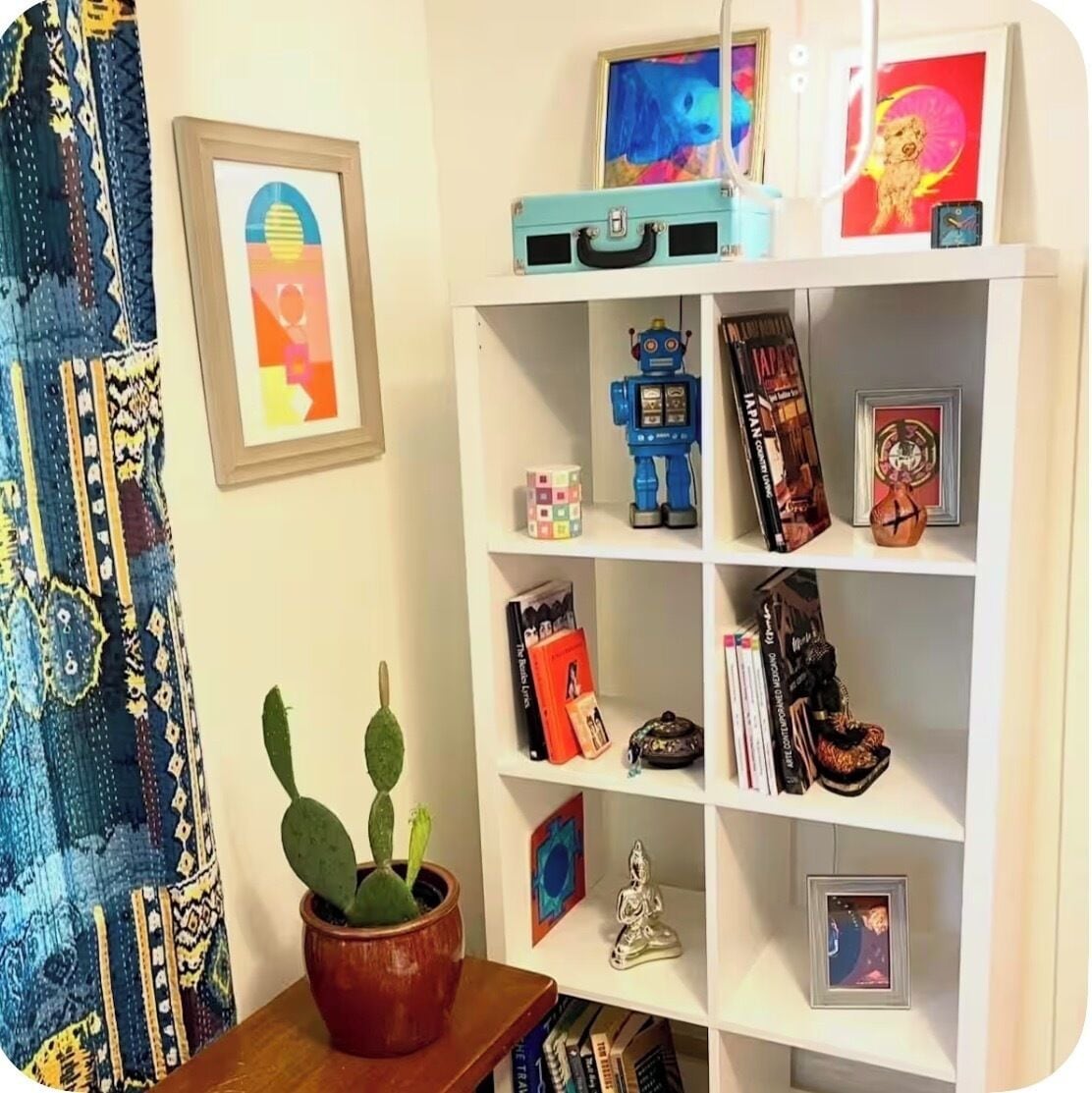 Een kamer met een witte boekenkast vol boeken, een blauw robot speeltje en ingelijste foto's.
