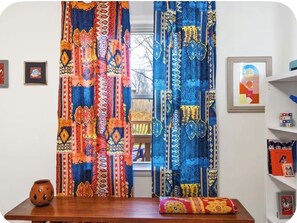 A room with a wooden table, a patterned curtain, and a shelf with books and decorative items. - A Home with a pulse (Charlotte)