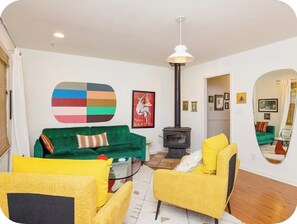 A living room with a green sofa, yellow armchairs, a black wood-burning stove, and a large mirror reflecting the room.