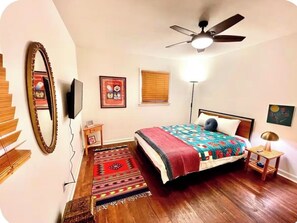 A bedroom with a bed, a ceiling fan, a TV, a mirror, and a window with blinds. - A Home with a pulse (Charlotte)