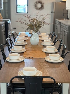 A dining table set with white plates and bowls, surrounded by chairs, with a vase of dried flowers in the center. - 3-Acre Wildlife Retreat : Sleeps & Dines 12 : 5 mi to Duncan: 26 mi to Fort Sill (Marlow)