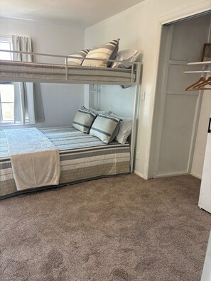 Ein Stockbett mit gestreifter Bettdecke und Kissen, einer weißen Decke und einem Teppichboden.