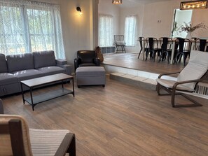 Ein modernes Wohnzimmer mit Sofa, Hocker, Couchtisch und einem Essbereich mit Stühlen und Tisch.
