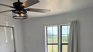 A bedroom with a bed, a ceiling fan, a window with curtains, and a view of the outdoors. - 3-Acre Wildlife Retreat : Sleeps & Dines 12 : 5 mi to Duncan: 26 mi to Fort Sill (Marlow)