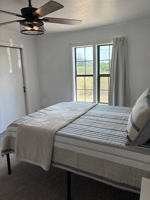 A bedroom with a bed, a ceiling fan, a window with curtains, and a view of the outdoors. - 3-Acre Wildlife Retreat : Sleeps & Dines 12 : 5 mi to Duncan: 26 mi to Fort Sill (Marlow)