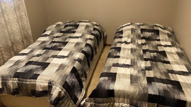 Two single beds with a checkered bedspread, a plain wall, and a curtain partially visible.