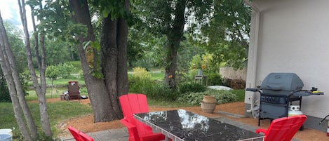 A patio with a table and chairs, a grill, and a garden in the background.