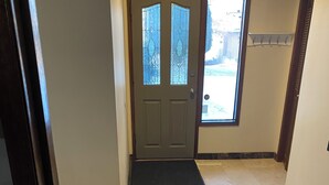 A hallway with a double door, a doormat, a tiled floor with a geometric pattern, and a wall-mounted coat rack.
