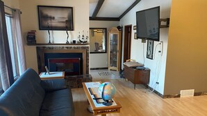 A living room with a fireplace, a television mounted on the wall, a sofa, a coffee table with a globe, and a wooden cabinet.