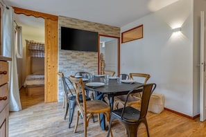 A dining area with a stone wall, a flat-screen TV, and a wooden dining table with chairs. - 40m from ski slopes, fitness, swimming pool, sauna, balcony, tv, ski locker, 43m², Les Orres (Les Orres)