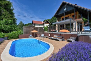 Een zwembad met ligbedden en parasols, omgeven door een aangelegde tuin met paarse bloemen.