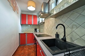 Een kleine keuken met rode kastjes, een zwart spoelgedeelte en een betegelde achterwand.