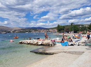 A beach with clear water, rocky outcrops, and people engaging in various water activities. - One Bedroom Apartment Lux 2 with Balcony (Okrug Gornji)