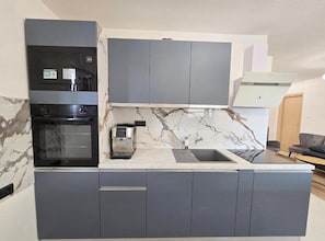 A modern kitchen with grey cabinetry, a built-in oven, a coffee machine, and a marble backsplash. - One Bedroom Apartment Lux 2 with Balcony (Okrug Gornji)