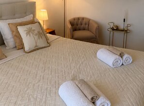 A neatly made bed with a quilted headboard, two pillows with palm tree designs, and two rolled towels on the bed. - One Bedroom Apartment with Sea View and Hydromassage Bath (Vodice)