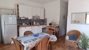 A compact kitchen with white cabinets, a refrigerator, a microwave, and a dining area with wicker chairs and a table. - Elegant vacation home in the Gulf of Asinara, ideal for families. (Sorso)