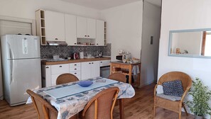 A compact kitchen with white cabinets, a refrigerator, a microwave, and a dining area with wicker chairs and a table. - Elegant vacation home in the Gulf of Asinara, ideal for families. (Sorso)