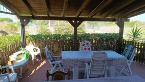 Een terras buiten met een houten pergola, een tafel met stoelen en een decoratieve afrastering.