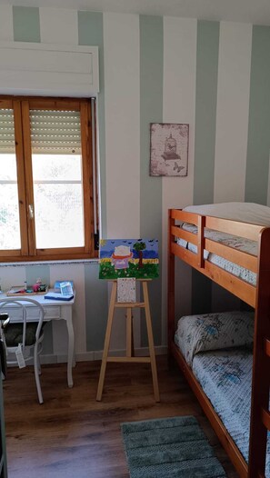Ein Zimmer mit einem Etagenbett, einem Schreibtisch mit Stuhl, einem Fenster mit Jalousien und einem Gemälde auf einem Staffelei.