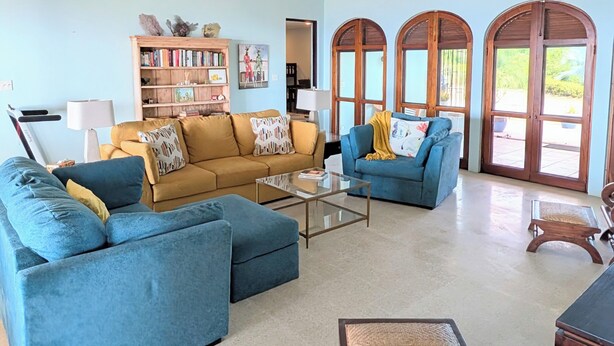 A spacious living room with a ceiling fan, a bookshelf, and a large window with arched doors.