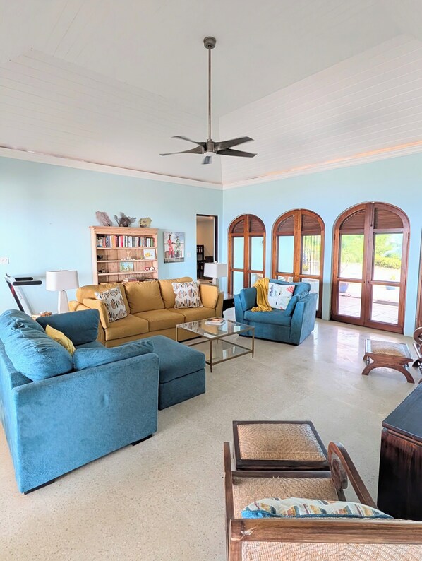 A spacious living room with a ceiling fan, a bookshelf, and a large window with arched doors.