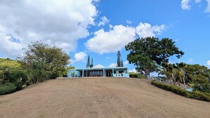 A house with a large lawn, a clear sky, and surrounding trees.