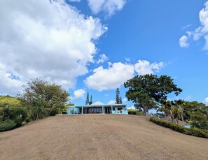 A house with a large lawn, a clear sky, and surrounding trees.