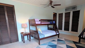 A bedroom with a bunk bed, a ceiling fan, a desk with a lamp, and a patterned rug.