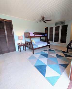 A bedroom with a bunk bed, a ceiling fan, a desk with a lamp, and a patterned rug.
