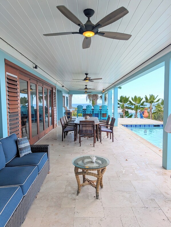 A covered outdoor area with a pool, a dining table with chairs, and a sofa.